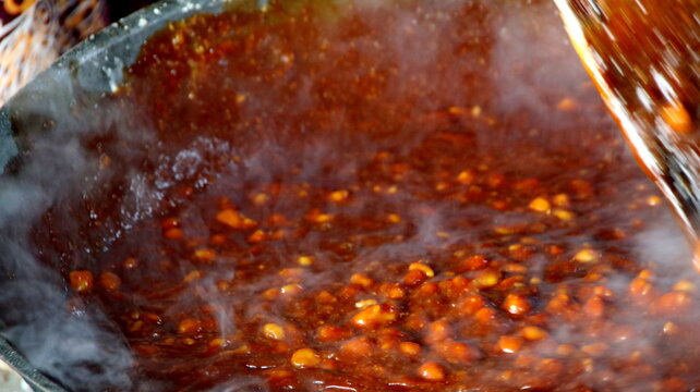 traditional maker stirs jenang gendul in a large wok over a wood fire, preparing the sweet delicacy inside a rustic Indonesian kitchen.