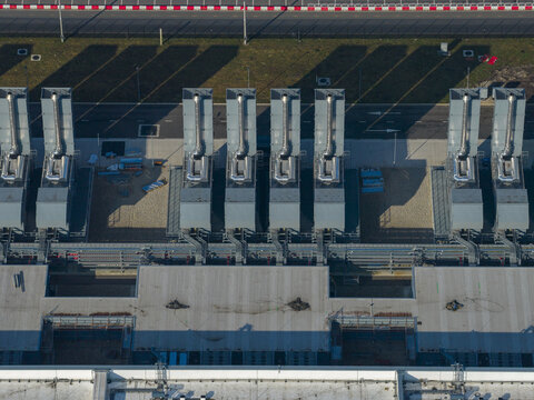Aerial view of an AI data center with cooling towers and cloud computing hub exterior featuring industrial exhaust stacks and long shadows on the ground.