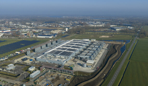 Aerial view of the Google data center with solar panels on the roof, surrounding green fields, and a canal under a clear blue sky in Winschoten, Groningen, Netherlands.