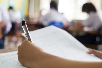 Obraz premium Close up hand of students reading and taking exam sheets exercises answer with stress in classroom
