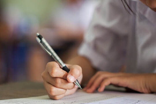 Close up hand of students reading and taking exam sheets exercises answer with stress in classroom