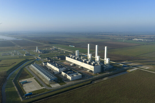 Aerial view of the nitrogen plant with tall white chimneys and industrial structures surrounded by flat agricultural fields in Zuidbroek, Groningen, Netherlands.