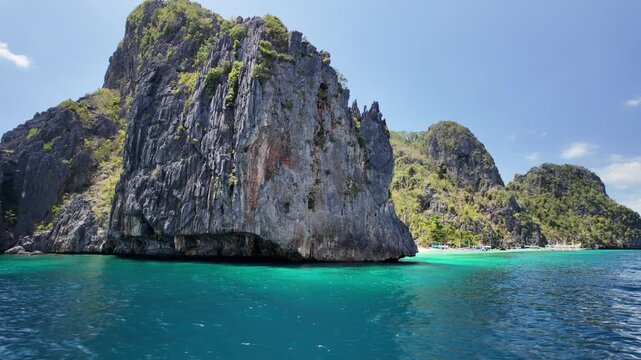 sea view of Entalula Beach, El Nido: limestone cliffs with lush greenery, white sand shore with boats and turquoise water under a bright blue sky, tranquil tropical paradise in Palawan, Philippines