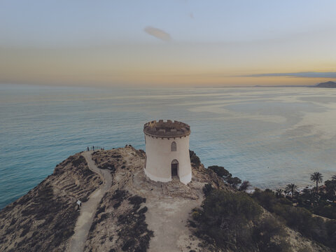 Aerial view of the Santuari iber i roma de la Malladeta tower on a rocky cliff overlooking the Mediterranean Sea at sunset in La Vila Joiosa, Comunidad Valenciana, Spain.