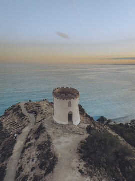 Aerial view of the Santuari iber i roma de la Malladeta tower perched on a rugged cliff overlooking the Mediterranean Sea at sunset in La Vila Joiosa, Comunidad Valenciana, Spain.