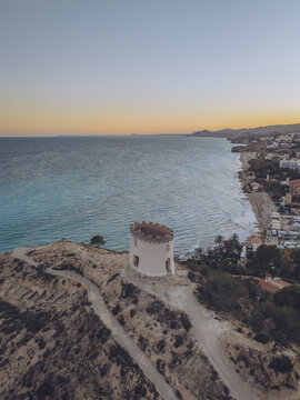 Aerial view of Santuari iber i roma de la Malladeta on a rocky cliff overlooking the Mediterranean coastline and sandy beaches at sunset La Vila Joiosa, Comunidad Valenciana, Spain.