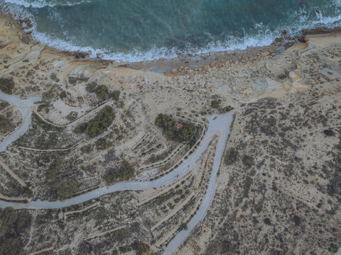 Aerial view of Santuari iber i roma de la Malladeta archaeological site with winding paths and rugged cliffs overlooking the turquoise sea, La Vila Joiosa, Comunidad Valenciana, Spain.
