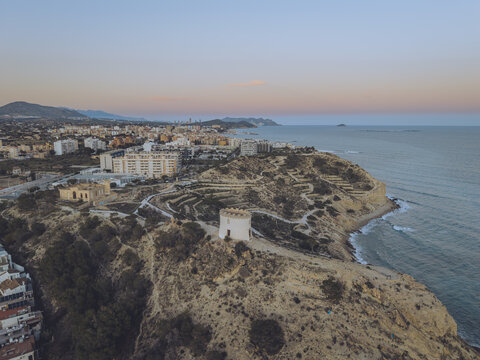 Aerial view of the Santuari iber i roma de la Malladeta tower on a rugged cliff overlooking the Mediterranean Sea at sunset in La Vila Joiosa, Comunidad Valenciana, Spain.