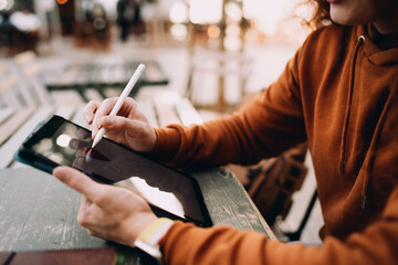 Detailed view of designer hands drawing on tablet screen with digital pen in outdoor setting....