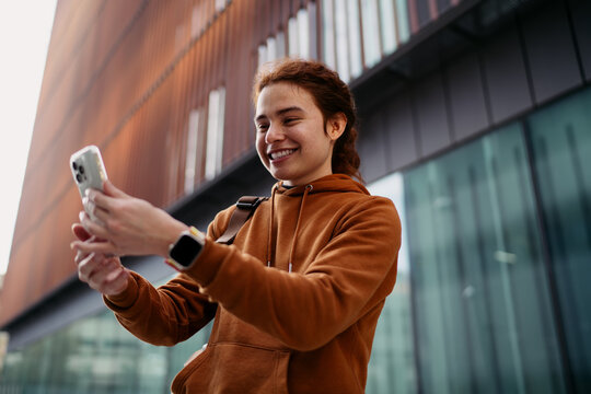 Happy woman holding smartphone with both hands looking at screen, receiving good news on mobile application, young digital nomad using 5G roaming service in modern city, lifestyle shot