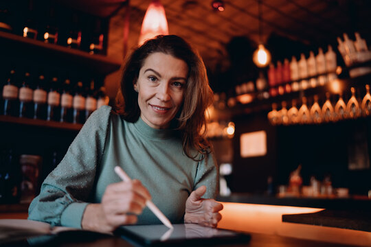 Portrait of Caucasian female professional using tablet with stylus, creative designer looking at camera at cafe, remote work and digital lifestyle, ambitious lady planning startup project.