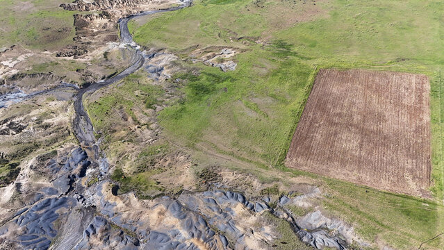 Aerial view of severe soil erosion and a dry riverbed next to a rectangular ploughed field in the rural landscape of Pietermaritzburg, KwaZulu-Natal, South Africa.