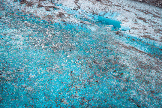 Close-up abstract of textured blue glacial ice with dark moraine sediment and frozen crystal patterns.