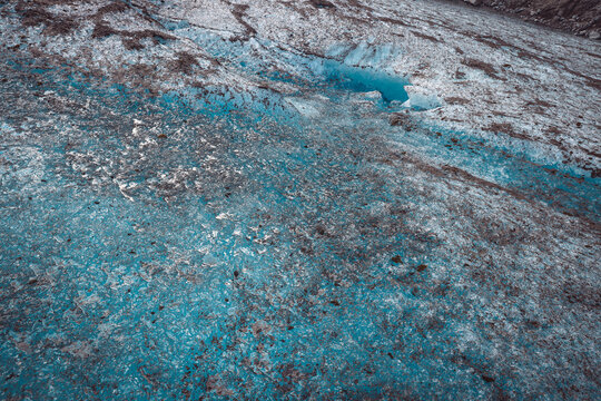 Close-up abstract of textured blue glacial ice with dark moraine sediment and frozen crystal patterns.