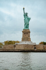 Fototapeta premium Statue of Liberty National Monument on Liberty Island NYC. Iconic green copper statue of Lady Liberty standing on pedestal against cloudy sky.