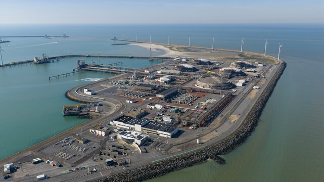 Aerial view of Fluxys LNG Terminal Zeebrugge featuring large storage tanks, industrial infrastructure, and wind turbines along the coast in Brugge, Vlaanderen, Belgium.