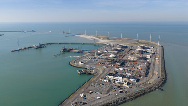 Aerial view of the Fluxys LNG Terminal Zeebrugge featuring storage tanks, industrial infrastructure, and wind turbines along the coastline in Brugge, Vlaanderen, Belgium.