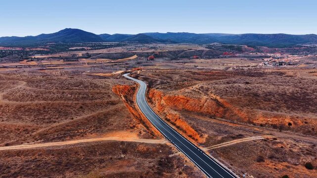 White car rides by the two-lane asphalt road along the dry rocky landscape. Drone flight over the arid scenery of Spain at daytime.