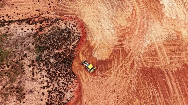 Excavator rides back and forth by the red sandstone landscape. Machinery working at the quarry. Top view.
