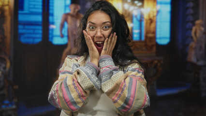Woman hands on head laughing with mouth open in museum building, wearing glasses, hoop earrings and patterned shirt  joy discovery. © Krakenimages.com