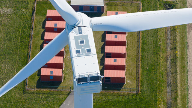 Aerial view of the nacelle and blades of a wind turbine at Energiepark Haringvliet Zuid with rows of red battery storage containers on green grass Middelharnis, South Holland, Netherlands.