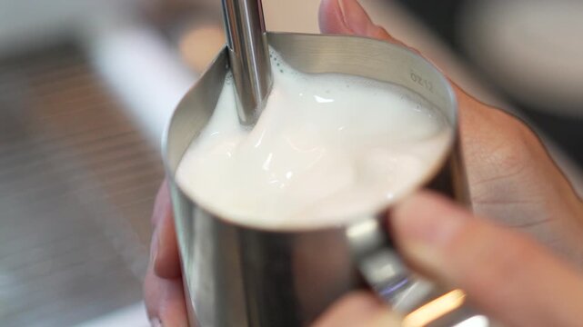Barista steaming milk close up of frothing milk in a stainless steel pitcher for latte art preparation