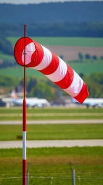 Red and white striped windsocks at airfield with airplanes on background, aviation weather monitoring for flight safety, airport wind direction indicator, navigation equipment for pilot guidance
