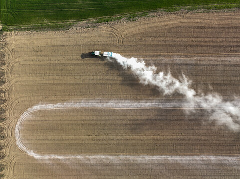 Aerial view of a tractor spreading white fertilizer across a tilled agricultural field with visible tire tracks Borgo d'Ale, Piedmont, Italy.