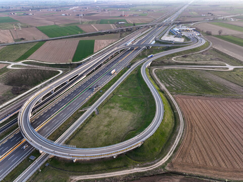 Aerial view of the Autostrada Torino Milano interchange with curved ramps and toll station surrounded by agricultural fields in Borgo d'Ale, Piedmont, Italy.