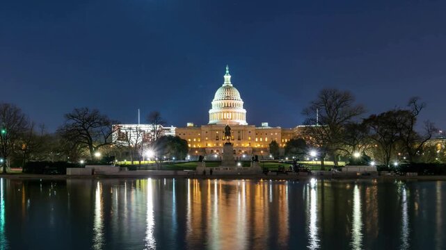 United states capitol building at night in washington dc viewed across reflecting pool with moon in sky and city lights shining on water during dusk.