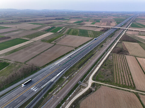 Aerial view of the A4 Torino-Milano motorway and parallel railway line crossing agricultural fields with vehicles in transit Borgo d'Ale, Piedmont, Italy.