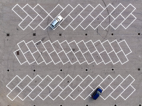 Aerial view of a parking lot with white diagonal lines and two cars parked on the asphalt in Borgo d'Ale, Piedmont, Italy.