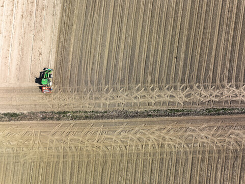 Aerial view of a green tractor working in a tilled agricultural field with geometric furrows and tire tracks in Rivalta di Torino, Piedmont, Italy.