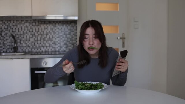 Young woman trying to lose weight before summer smells chocolate while eating low calorie salad using funny self control trick at home kitchen