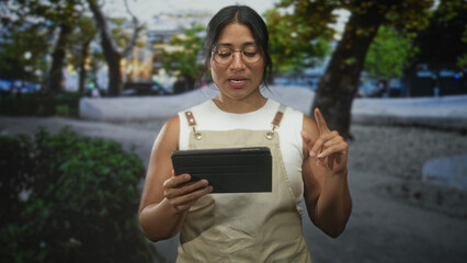 Woman in apron holding a tablet and gesturing with her hand on a street plaza, reading and tapping the screen  focus. © Krakenimages.com