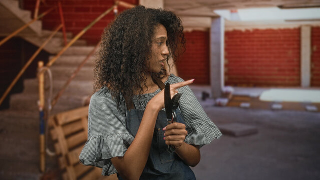 Woman waitress holding cutlery points finger while holding utensils in a brick building interior; caution.