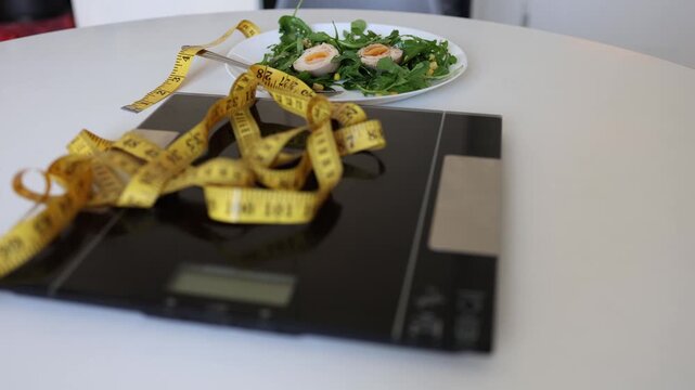 Bathroom scale and measuring tape dominate a healthy salad scene showing how weight loss pressure can turn simple meals into body anxiety and restrictive diet control now