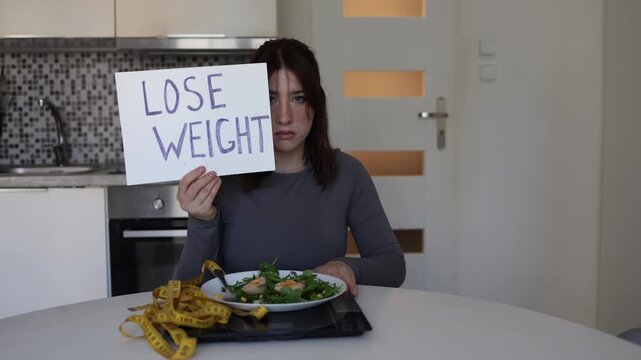 Young woman holds a lose weight sign beside salad scale and measuring tape showing diet pressure body image anxiety and how strict food rules can drain self worth today
