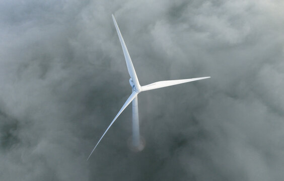 Aerial view of a single white wind turbine emerging from a thick layer of morning fog and low clouds in Netherlands.