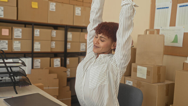 Woman stretches hands over laptop amid cardboard boxes in a delivery office building; small business relief.