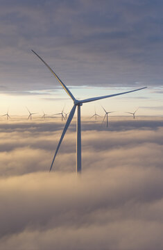 Aerial view of wind turbines rising above a thick layer of clouds during a golden sunrise in Netherlands.