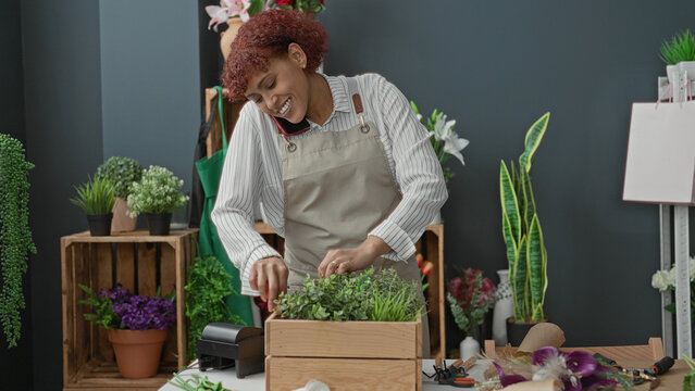 Woman florist arranging potted plants with hands and phone to cheek in building; careful multitasking calm.