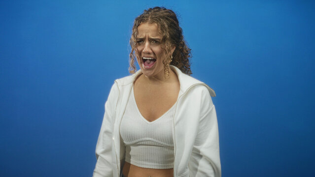 Woman with visible cleavage in white crop top and hoodie, mouth open shouting in studio; raw frustration.