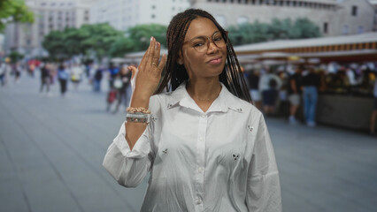 Obraz premium Woman points finger to ring on left hand at busy street market stalls in outdoor city plaza, wearing glasses and bracelets; personal pride.