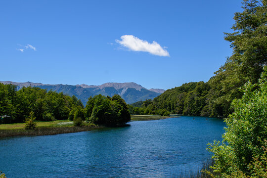 Hermosa vista del r&iacute;o Manso conectando lagos Hess, rodeado de frondosos bosques nativos y la cordillera de fondo bajo un cielo azul, Patagonia, Argentina.