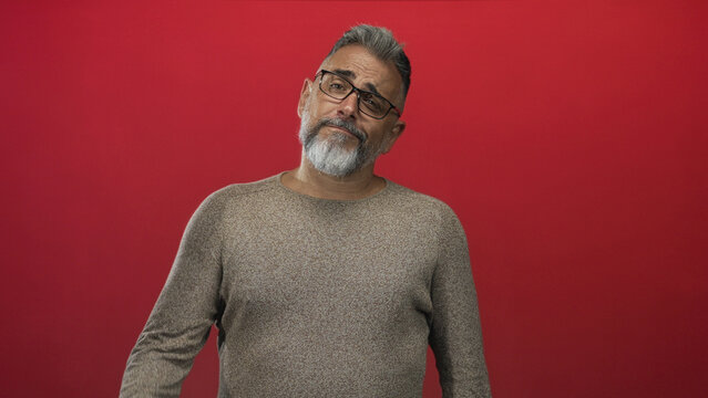 Middle aged man arms crossed showing forearms and beard, wearing glasses in studio with red wall; warm confidence.