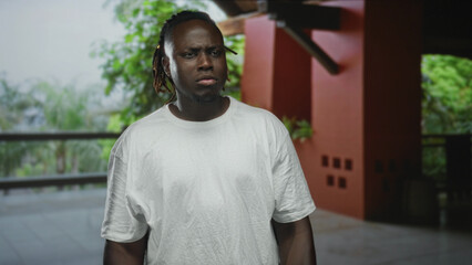 Fototapeta premium Young man with furrowed brow and visible face at building balcony wearing white t shirt; concern reflection.