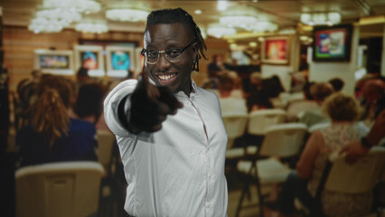 Obraz premium Man making peace sign and pointing finger in studio gallery among seated audience; joy celebration together.