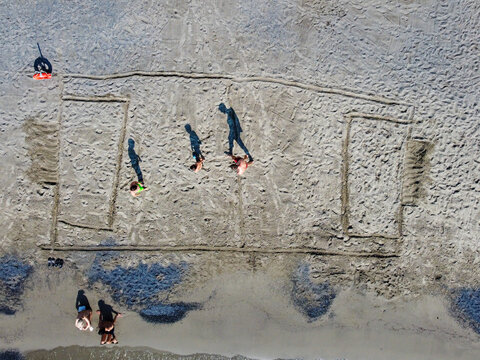 Aerial view of a soccer field outline drawn in the sand with people walking on the beach in San Lorenzo, Liguria, Italy.