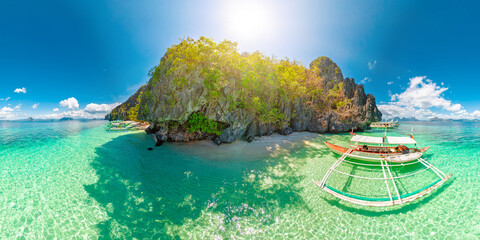 Entalula Beach in El Nido, Philippines, limestone cliffs, vibrant tropical vegetation, and traditional outrigger boats floating on crystal-clear turquoise waters under sunny blue sky of Palawan island © bennymarty